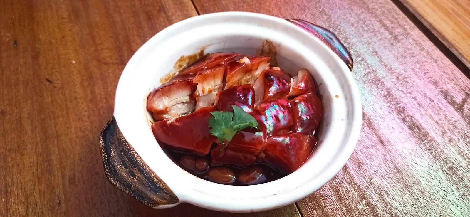 A small clay pot of Dong Po pork belly with peanuts and coriander on a wooden table