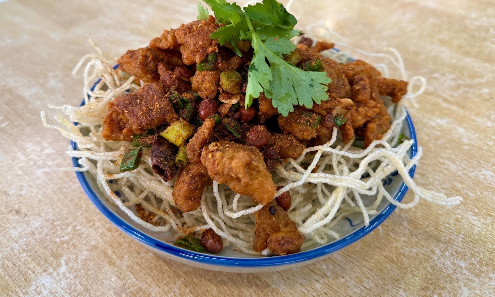 Spicy fried pork slices piled on crispy fried vermicelli with coriander